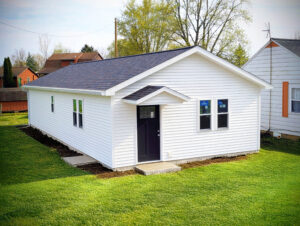 White vinyl-sided tiny home shell with black front door and shingle roof.